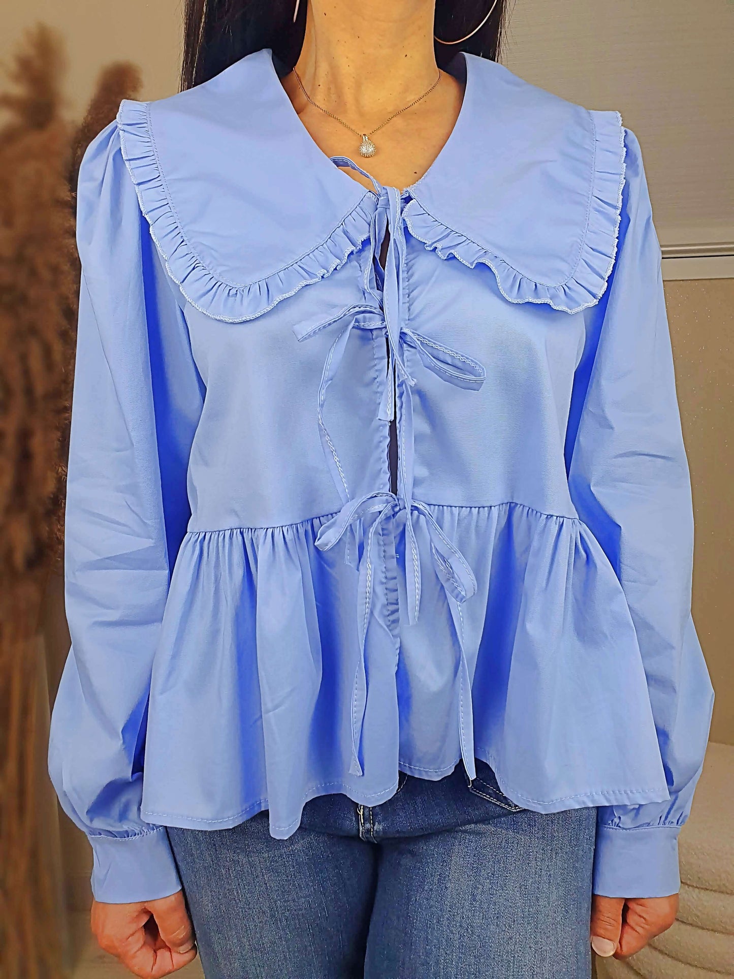Découvrez notre blouse bleue à nouer devant pour femme, avec un col claudine. Ses manches longues et bouffantes sont dotées d'un bouton, et sa coupe légèrement évasée sur le bas apporte une touche élégante. Fermeture avec 3 nœuds sur l'avant. Confectionnée en 100% coton et fabriquée en Italie, elle allie style et confort.