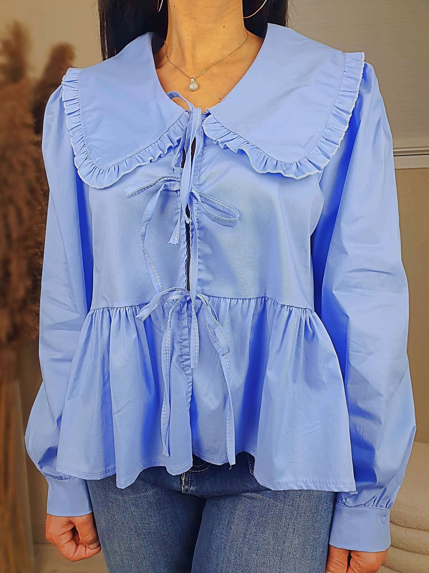 Découvrez notre blouse bleue à nouer devant pour femme, avec un col claudine. Ses manches longues et bouffantes sont dotées d'un bouton, et sa coupe légèrement évasée sur le bas apporte une touche élégante. Fermeture avec 3 nœuds sur l'avant. Confectionnée en 100% coton et fabriquée en Italie, elle allie style et confort.