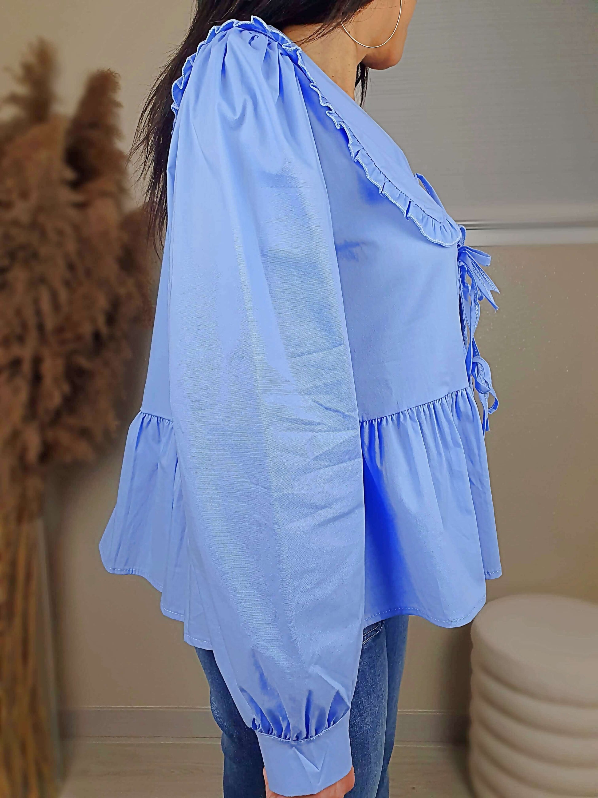 Découvrez notre blouse bleue à nouer devant pour femme, avec un col claudine. Ses manches longues et bouffantes sont dotées d'un bouton, et sa coupe légèrement évasée sur le bas apporte une touche élégante. Fermeture avec 3 nœuds sur l'avant. Confectionnée en 100% coton et fabriquée en Italie, elle allie style et confort.