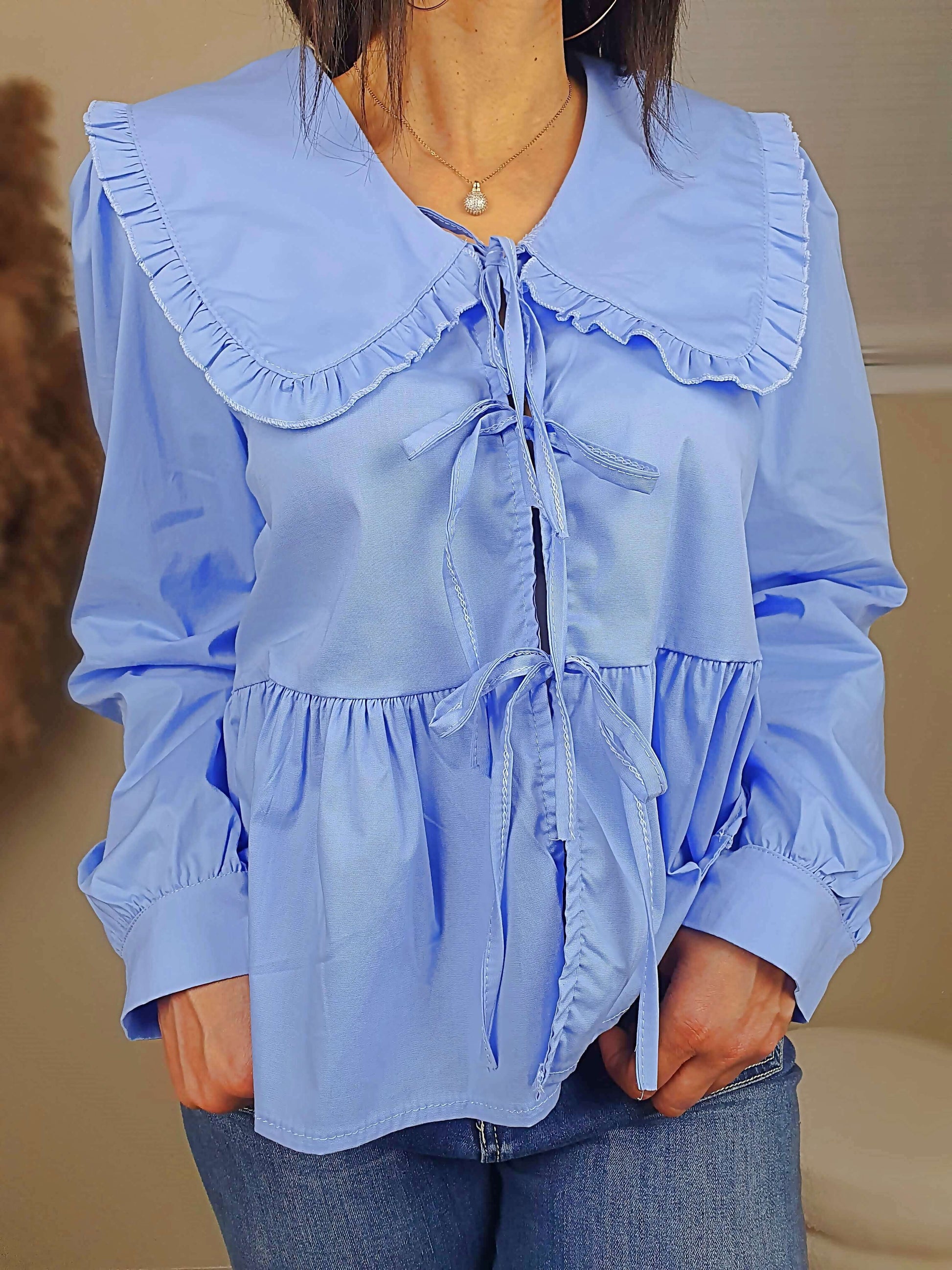Découvrez notre blouse bleue à nouer devant pour femme, avec un col claudine. Ses manches longues et bouffantes sont dotées d'un bouton, et sa coupe légèrement évasée sur le bas apporte une touche élégante. Fermeture avec 3 nœuds sur l'avant. Confectionnée en 100% coton et fabriquée en Italie, elle allie style et confort.