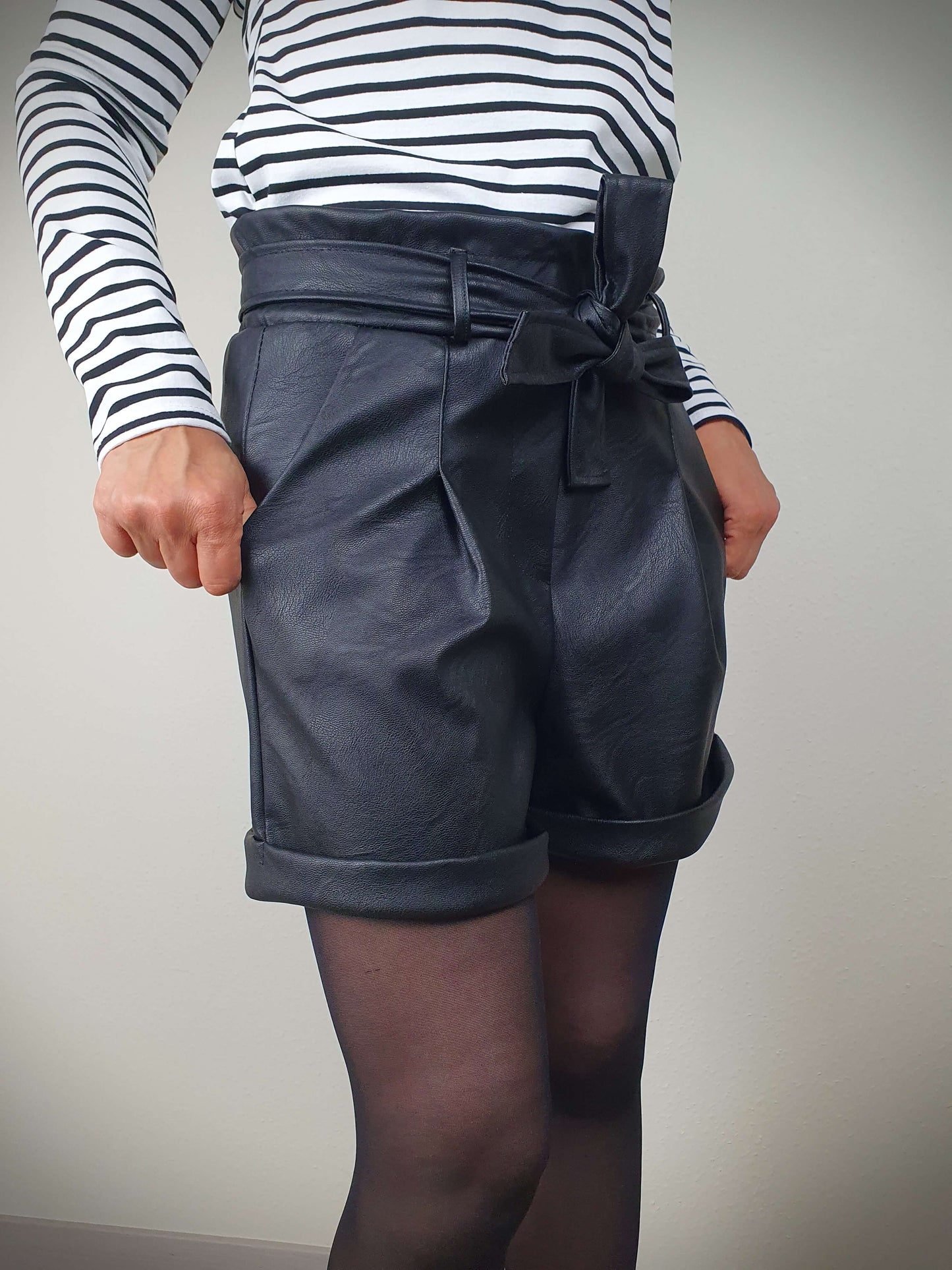 Découvrez ce court en simili cuir noir pour femme, avec une coupe droite flatteuse, taille élastiquée, ceinture à nouer et poches italiennes. Les pinces avant offrent une silhouette élégante, tandis que les revers ajoutent une touche tendance. Fabriqué en Italie avec 45% polyester et 55% polyuréthane pour une qualité exceptionnelle.