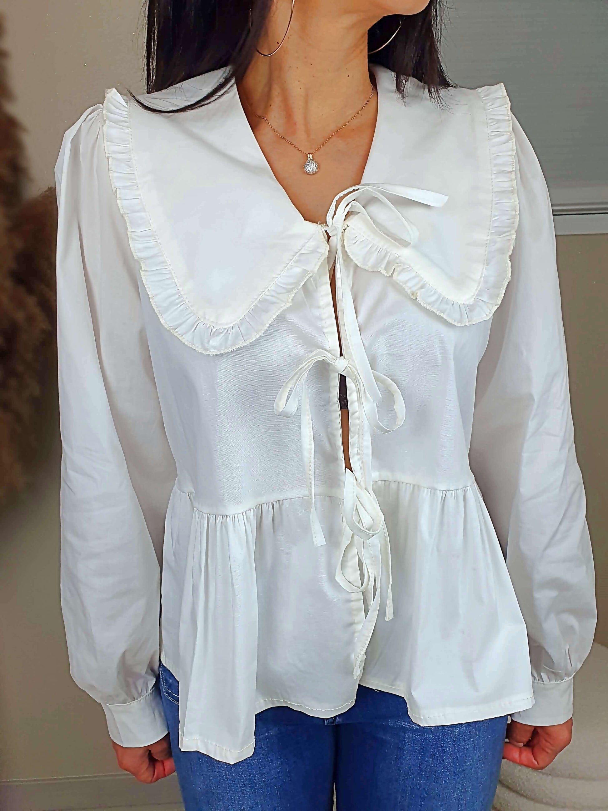Découvrez notre blouse blanche à nouer devant pour femme, avec un col claudine. Ses manches longues et bouffantes sont dotées d'un bouton, et sa coupe légèrement évasée sur le bas apporte une touche élégante. Fermeture avec 3 nœuds sur l'avant. Confectionnée en 100% coton et fabriquée en Italie, elle allie style et confort.