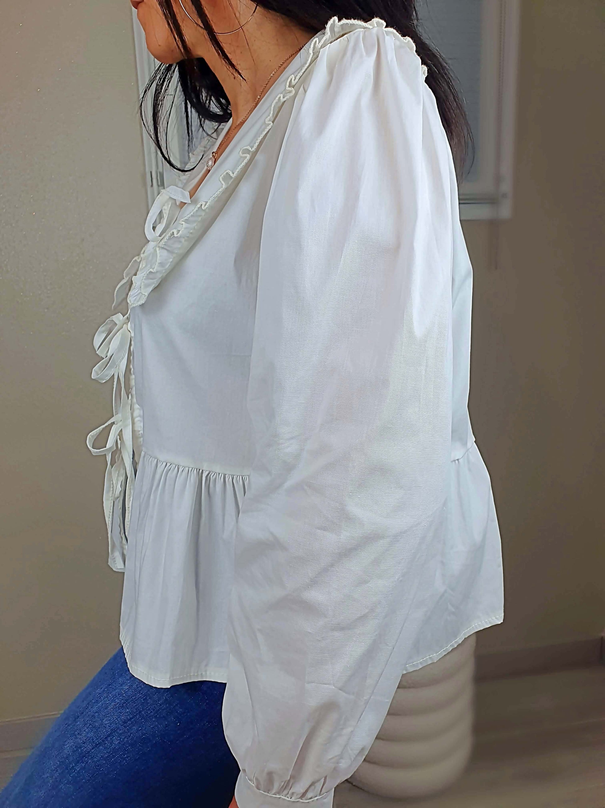 Découvrez notre blouse blanche à nouer devant pour femme, avec un col claudine. Ses manches longues et bouffantes sont dotées d'un bouton, et sa coupe légèrement évasée sur le bas apporte une touche élégante. Fermeture avec 3 nœuds sur l'avant. Confectionnée en 100% coton et fabriquée en Italie, elle allie style et confort.